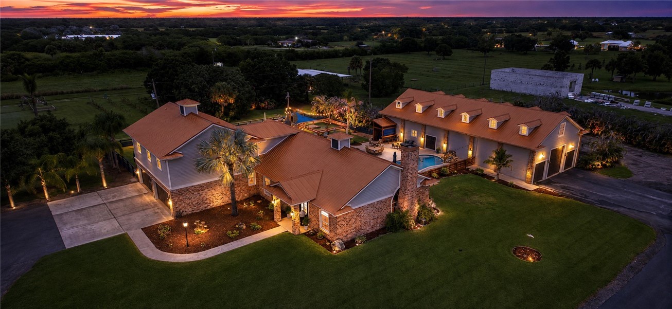 Expansive property featuring multiple structures with complementary metal roofs, a large patio with built-in pool, extensive hardscaping, and mature landscaping