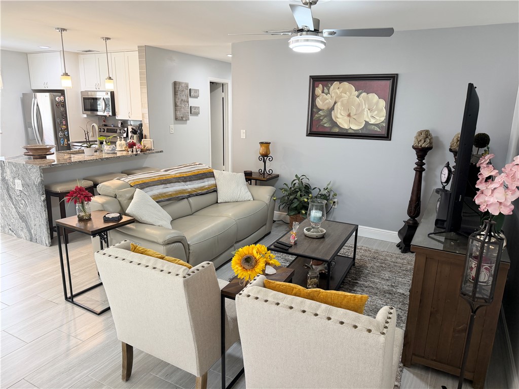 Open-concept living space featuring a kitchen with stainless steel appliances, white cabinetry, and a stone-finish breakfast bar
