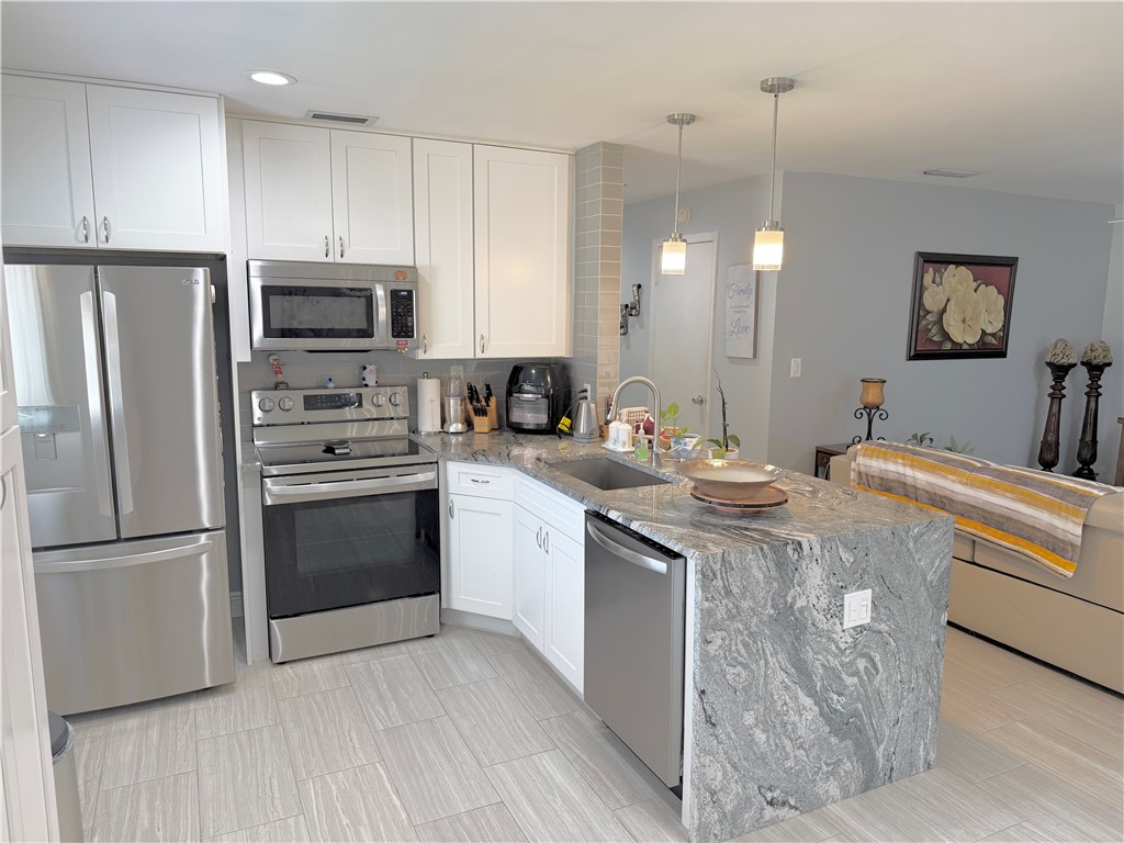 Kitchen featuring white cabinetry, stainless steel appliances, a waterfall island with an undermount sink, and light-toned tile flooring
