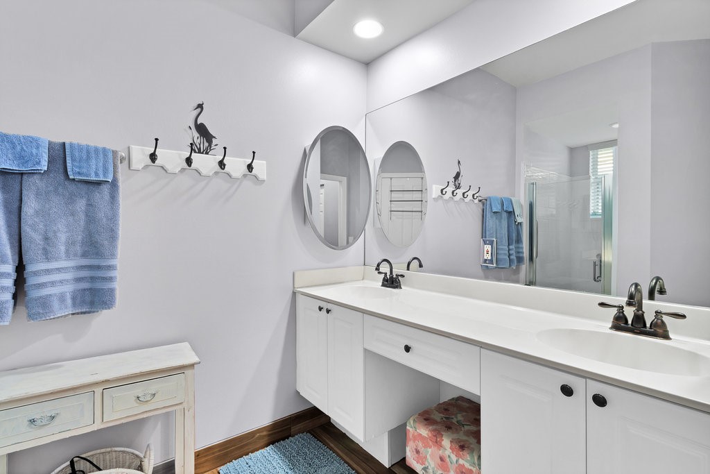 Dual vanity with integrated sinks, expansive wall-mounted mirror, white cabinetry, and wood-finish flooring