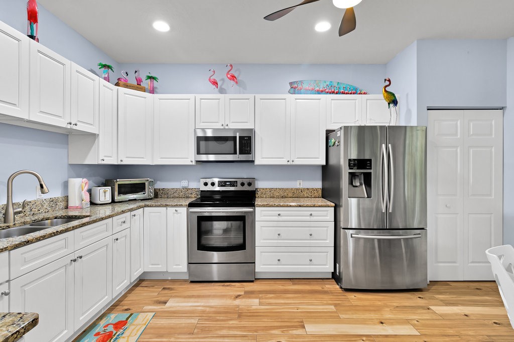 White cabinetry with brushed nickel hardware, granite countertops, stainless steel appliances, wood-finish flooring, and recessed lighting