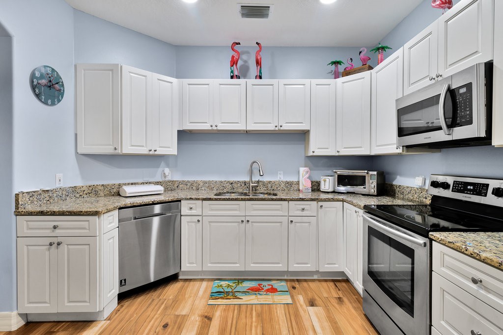 Kitchen featuring white cabinetry, light-toned countertops, wood-finish flooring, stainless steel appliances, and a stainless steel sink