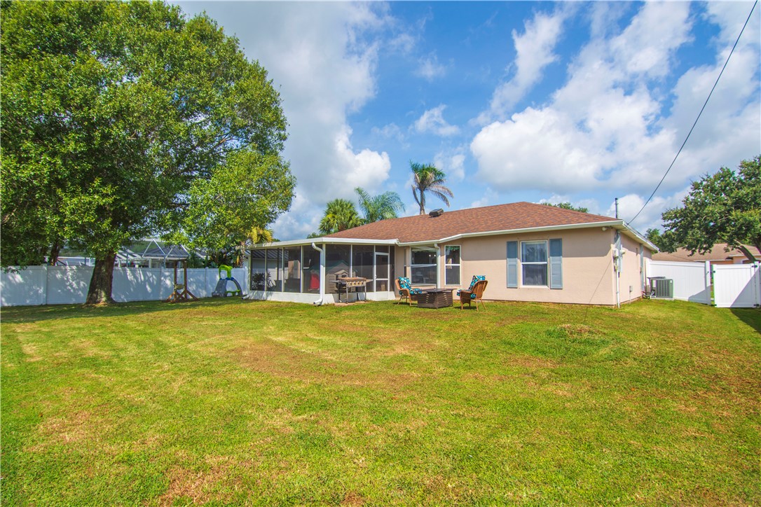 Expansive backyard featuring a screened patio, mature trees, and a white privacy fence