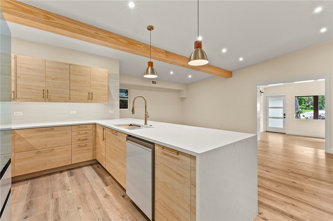 Modern kitchen featuring wood-finish cabinetry, white countertops, and a central island with an integrated sink and gooseneck faucet