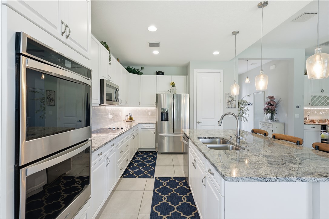 Gourmet kitchen featuring a large island with sink, stainless steel appliances, white cabinetry, granite countertops, and tiled flooring