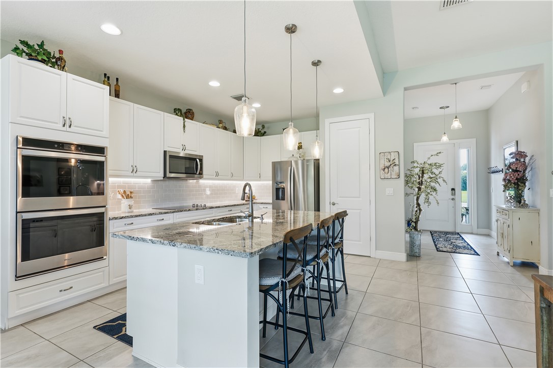 Spacious kitchen featuring an oversized island with granite countertops, white shaker cabinetry, stainless steel double ovens, and a subway tile backsplash