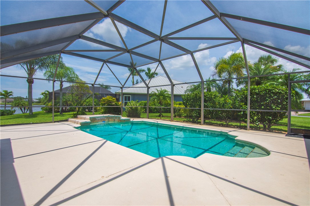 Screened pool enclosure featuring a rectangular pool with integrated steps, a spa with a waterfall feature, and a neutral-toned pool deck