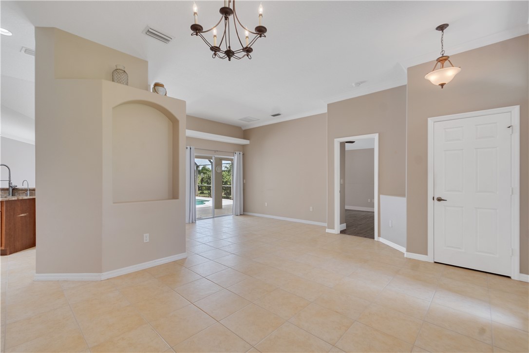 Spacious interior featuring neutral tone walls, tile flooring, crown molding, a decorative arch niche, and a bronze chandelier