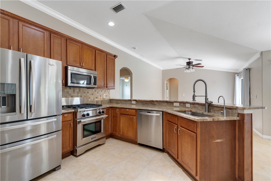 Kitchen featuring wood cabinetry, stainless steel appliances, a multi-tone tile backsplash, and stone countertops