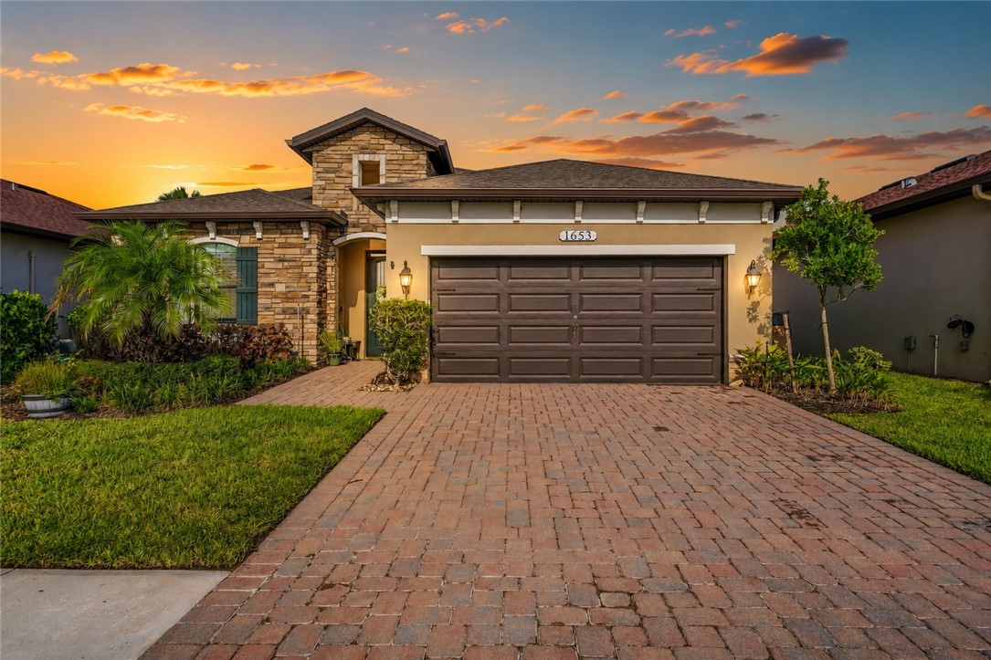 Stucco and stone facade home featuring a two-car garage, brick paver driveway, and professional landscaping