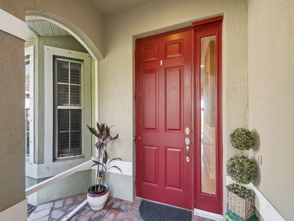 Entryway featuring a paneled red door with sidelight, bay window with louvered shutters, and brick paver flooring