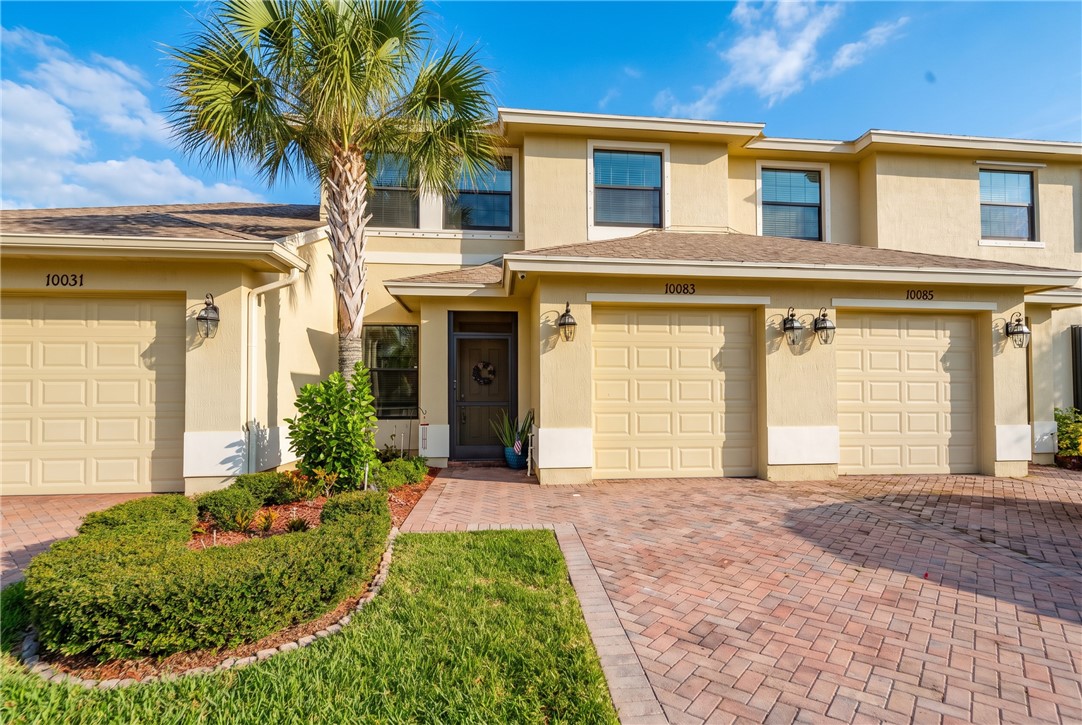Stucco exterior with multiple garage entrances, a paver driveway, and a mature palm tree