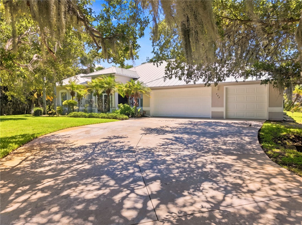 Concrete driveway leading to a residence with a light-colored exterior and a metal roof