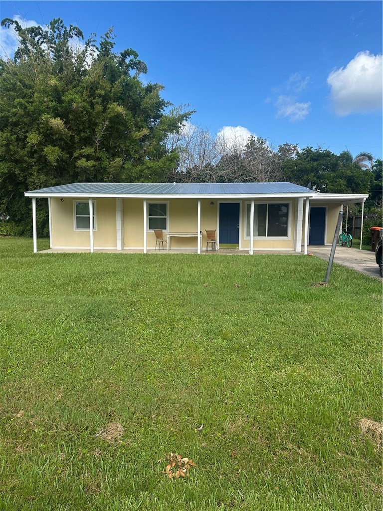 Single-story residence featuring a covered front porch spanning the width of the home, a light-yellow exterior, a blue metal roof, and a large front lawn