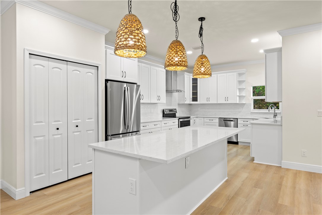 Kitchen featuring an island with a light-toned countertop, white cabinetry, stainless steel appliances, and woven pendant lighting