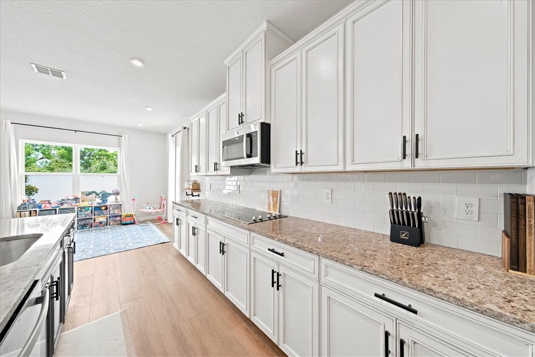 Contemporary kitchen featuring white cabinetry, a built-in microwave, light-toned wood-finish flooring, and a subway tile backsplash