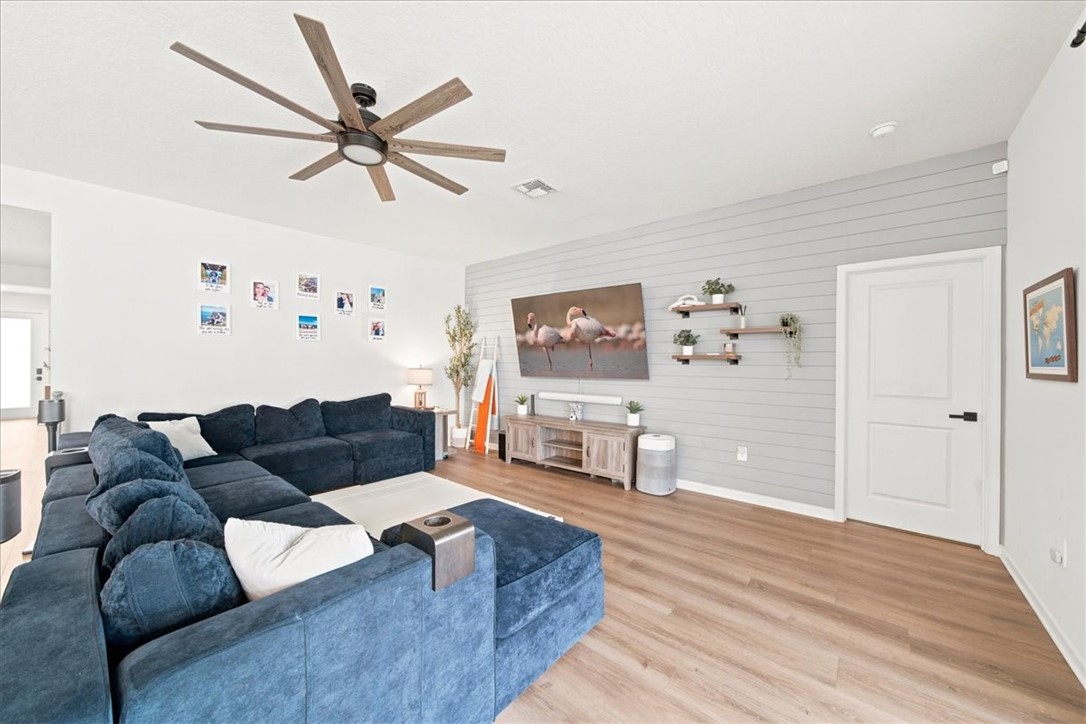Spacious living area featuring wood-finish flooring, a contemporary ceiling fan, and a shiplap accent wall