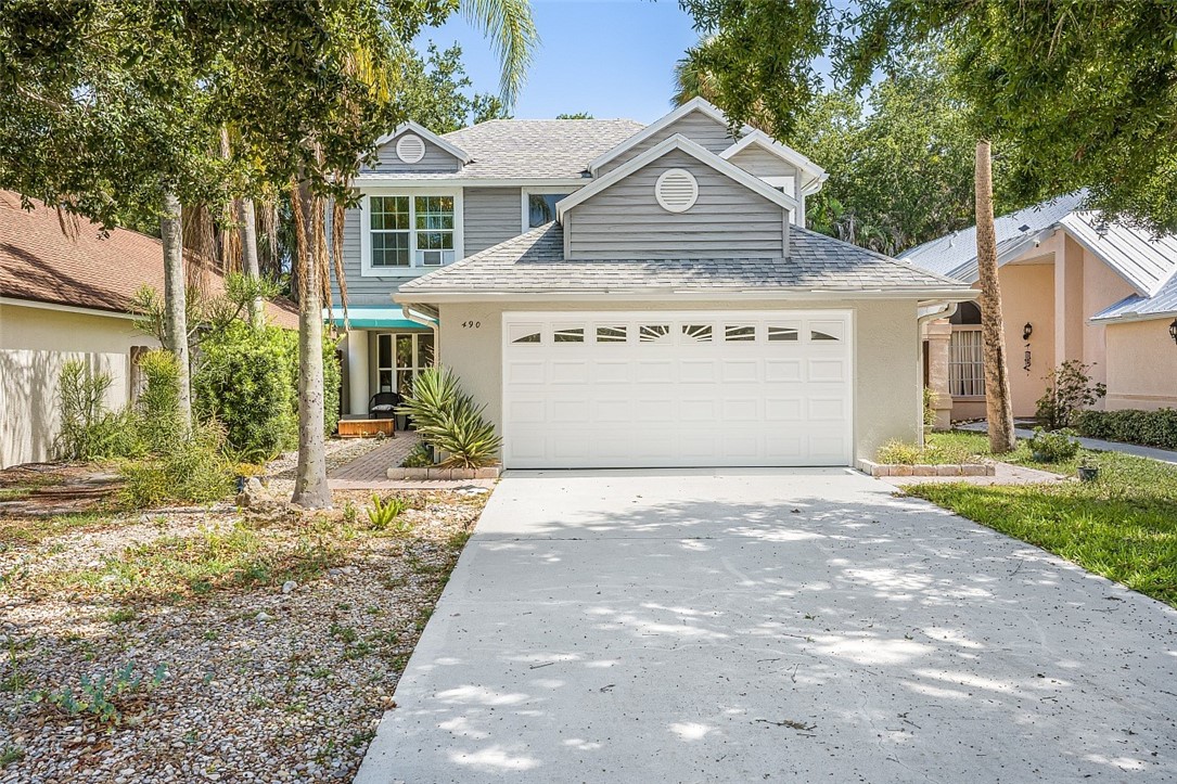 Two-story residence featuring a two-car garage with white door, light gray siding, and a shingled roof