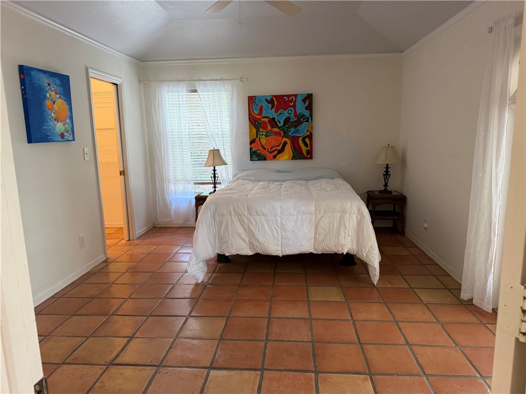 Room featuring terracotta-style tile flooring, a vaulted ceiling, and crown molding