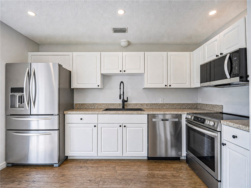 Kitchen featuring wood-finish flooring, white cabinetry with black hardware, and speckled countertops