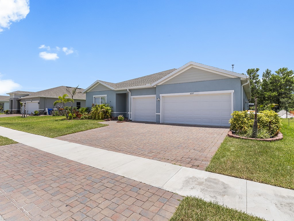 Contemporary stucco exterior featuring a two-car garage, paver driveway, and mature landscaping