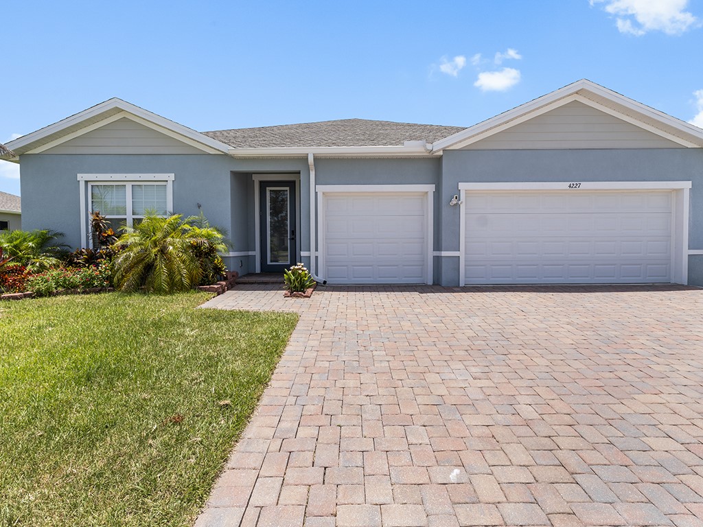 Single-story residence featuring a two-car garage, light blue stucco exterior, and a paver driveway