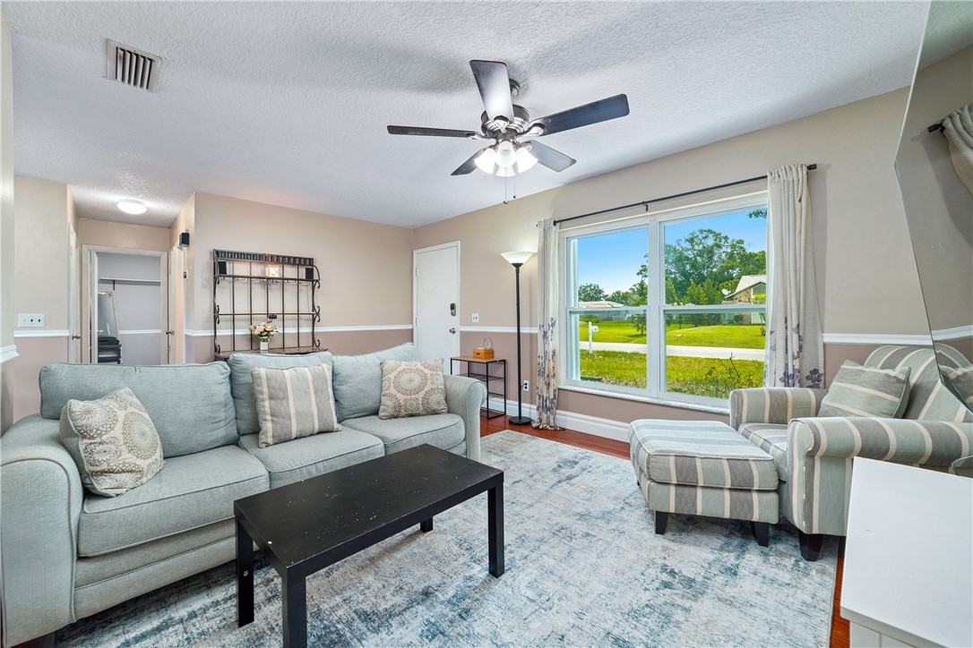 Living area featuring a ceiling fan, wood-finish flooring, and a large window