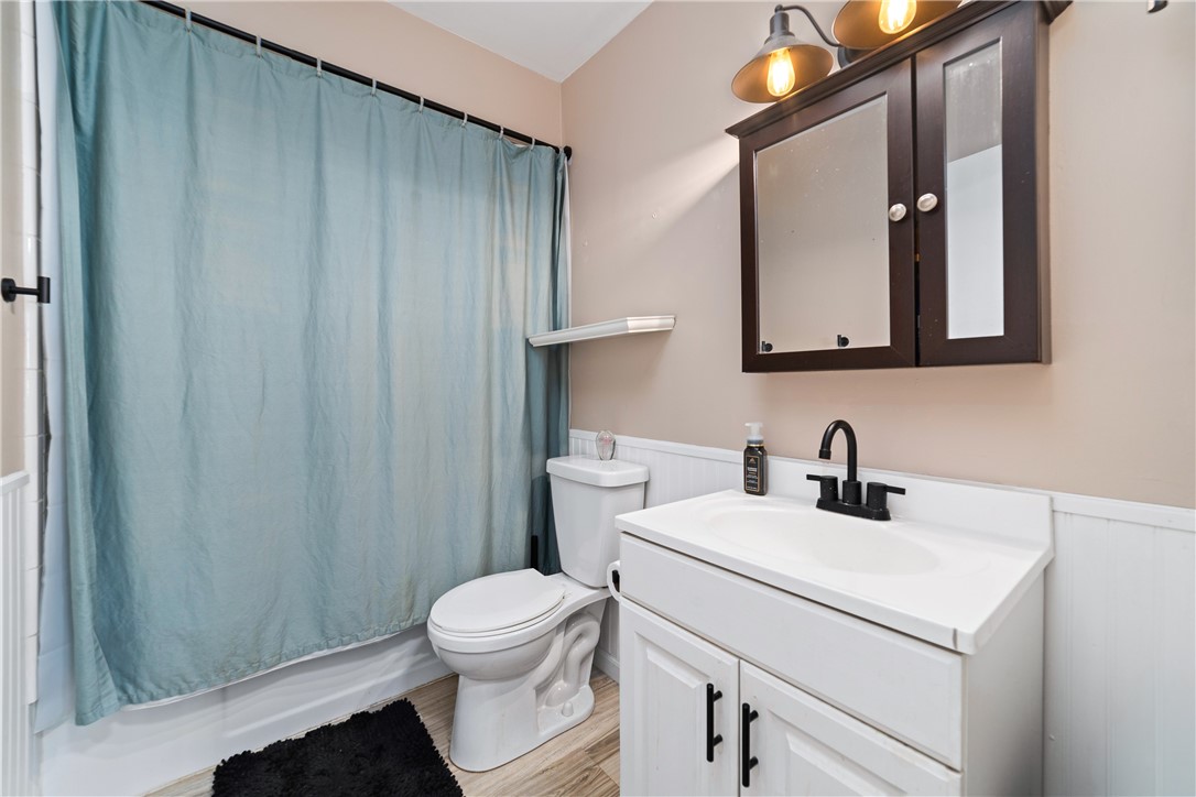 Bathroom featuring a white vanity with a single basin sink, matte black faucet, wood-finish flooring, and white wainscoting