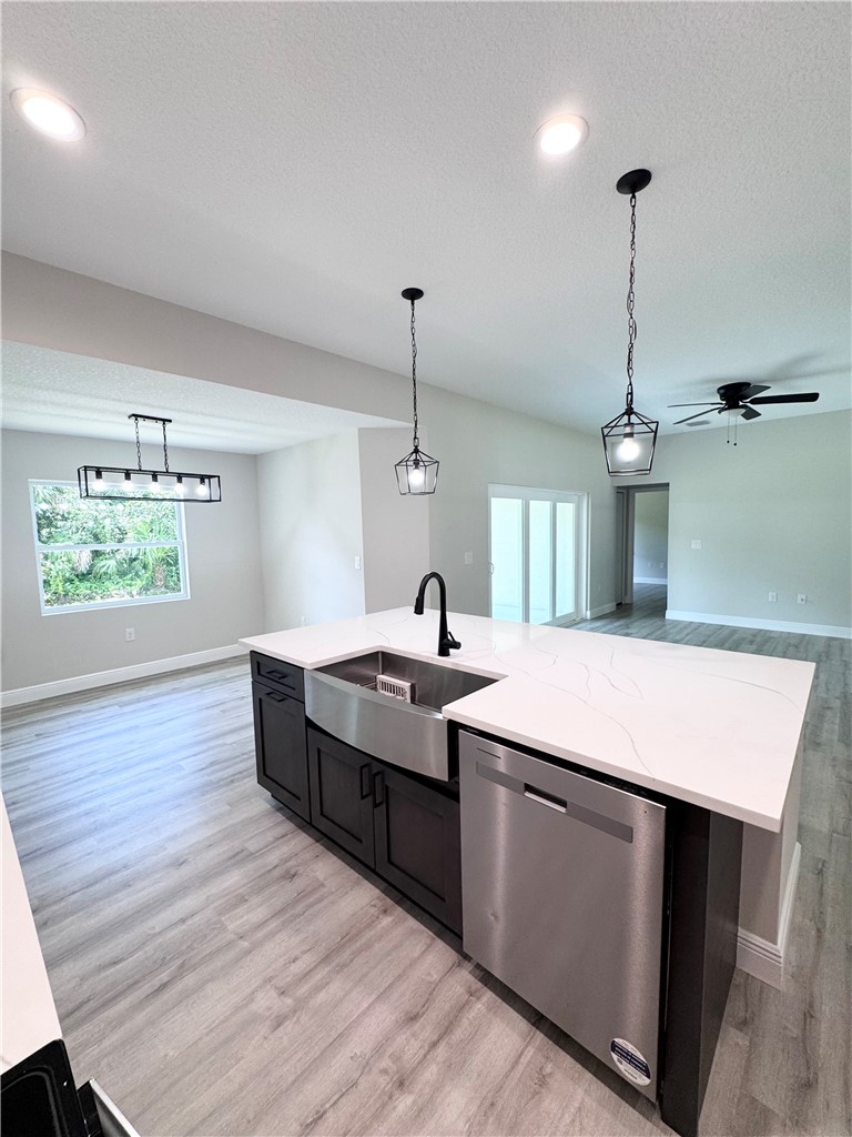 Modern kitchen island featuring a farmhouse-style apron sink with matte black faucet, stainless steel dishwasher, white quartz countertops, and dark cabinetry with open shelving