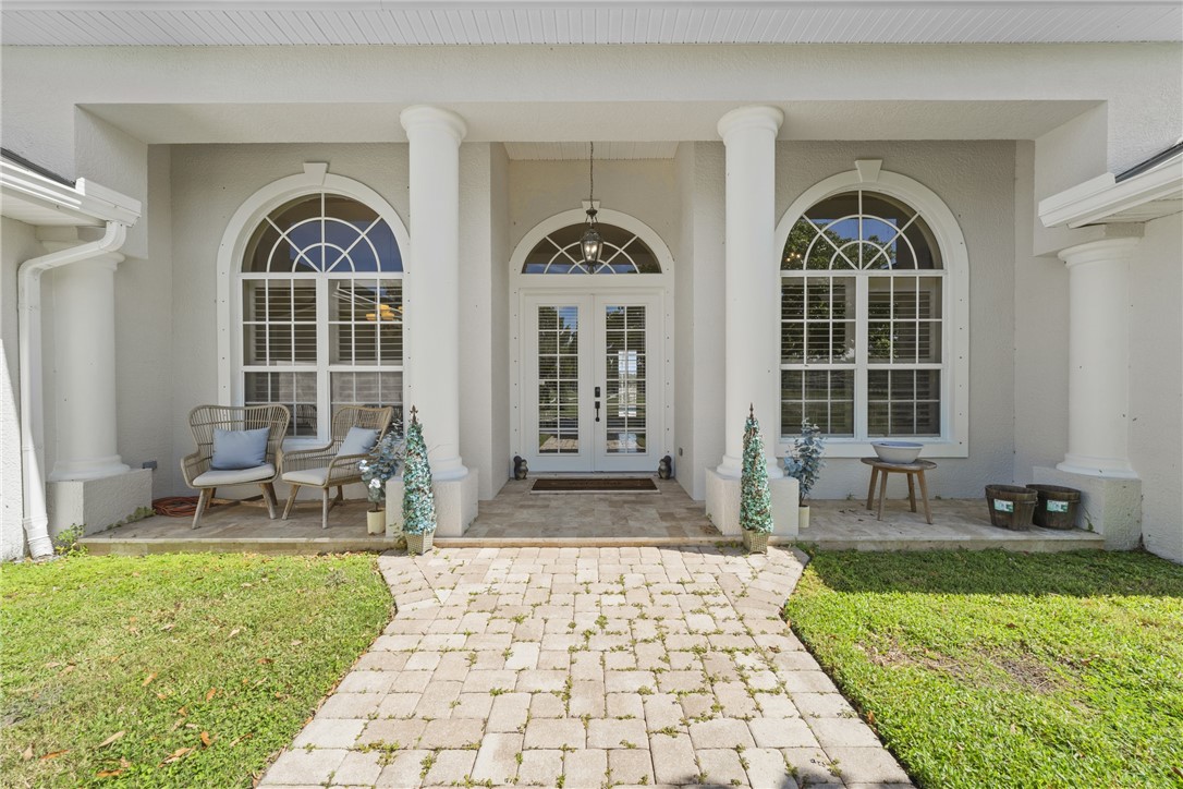 Covered entryway with architectural columns, arched windows, and a paver stone walkway