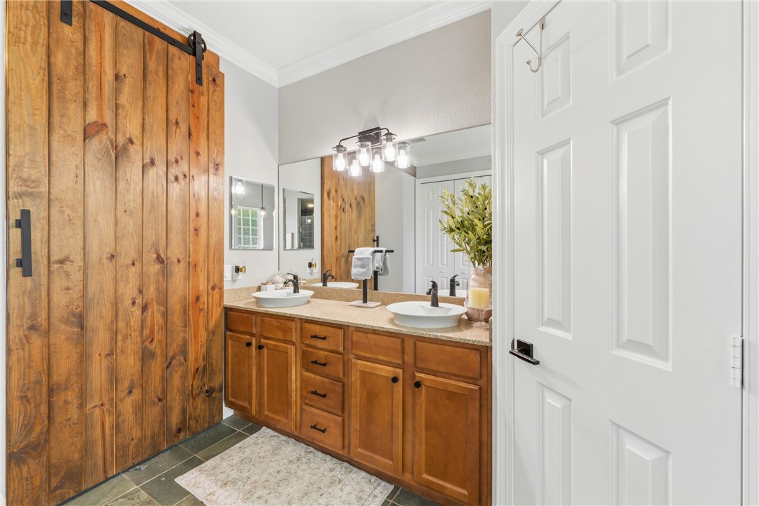 Dual vanity with vessel sinks, wood-finish cabinetry, full-width mirror, industrial-style vanity lighting, and a wood-paneled barn door