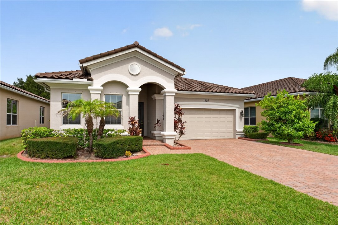 Stucco exterior with a tile roof, featuring a paver driveway, an arched entry, and a two-car garage
