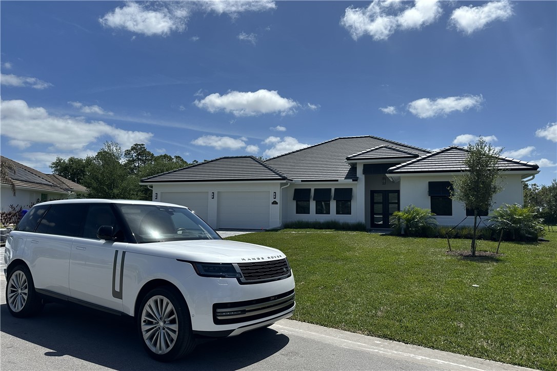 Modern white exterior featuring a flat tile roof, black frame impact windows with a three-car garage