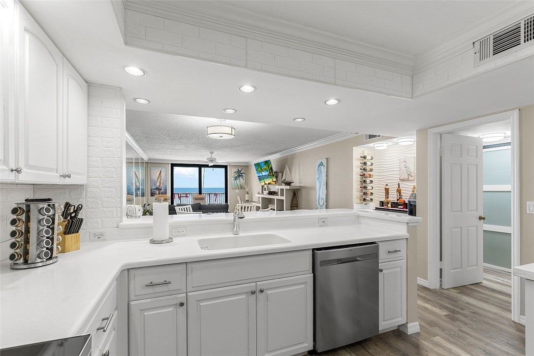 White cabinetry with brushed nickel hardware, integrated sink, stainless steel dishwasher, recessed lighting, and wood-finish flooring