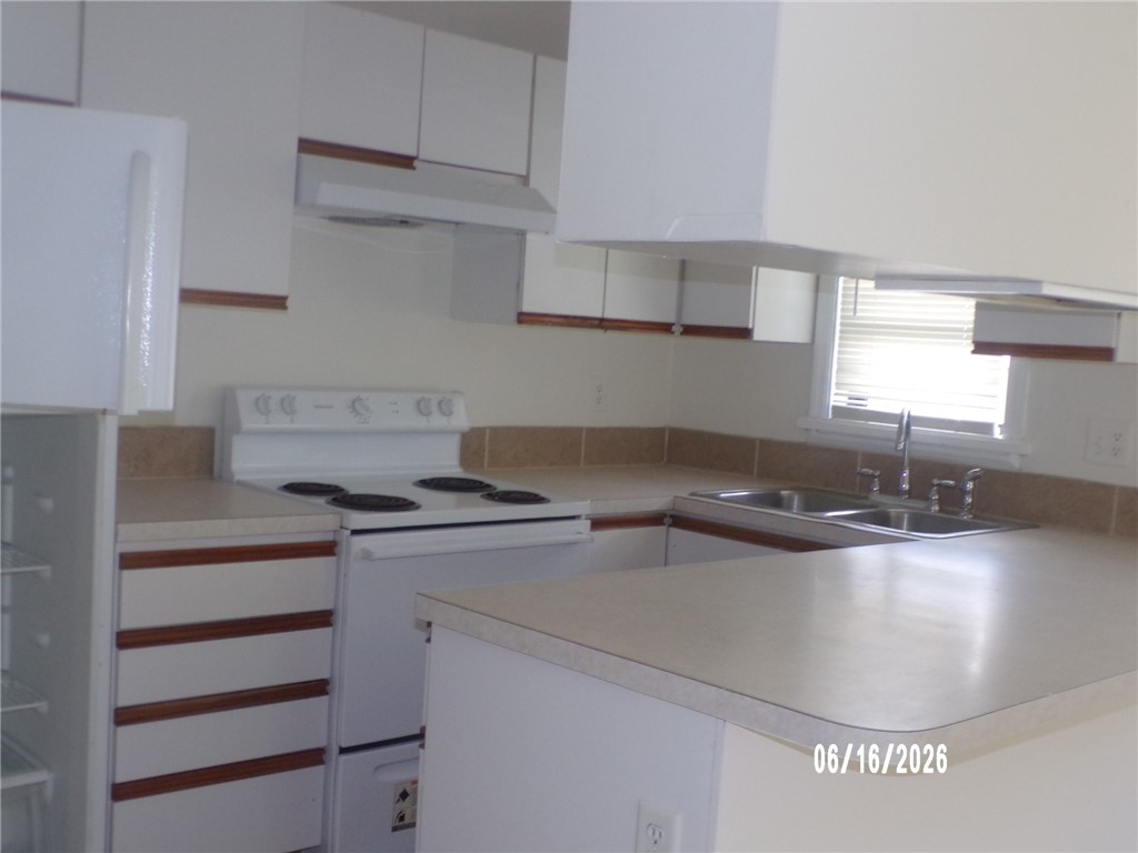 Kitchen featuring white cabinetry, light-toned countertops, a built-in double basin sink, and a white electric range with an overhead hood