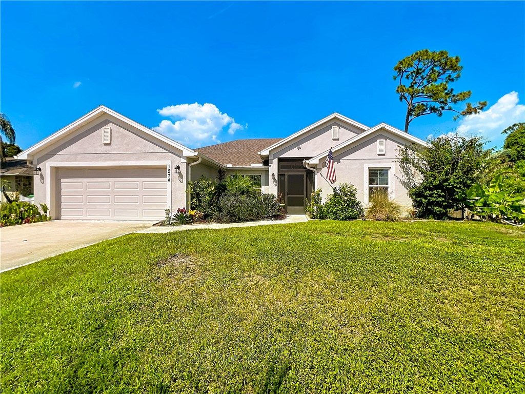 Stucco exterior with a pitched roofline, attached garage, screened entry, and established landscaping