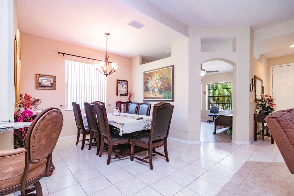 Dining area featuring light-toned tile flooring, a window with vertical blinds, and a decorative chandelier