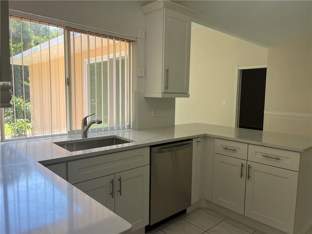 Modern kitchen featuring light countertops, white shaker-style cabinetry, and a stainless steel dishwasher
