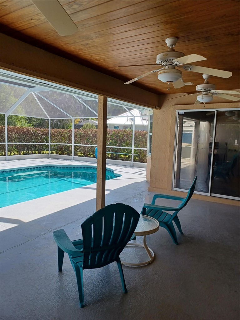Screened-in pool area featuring a covered patio with wood-finish ceiling, two ceiling fans, a turquoise swimming pool, and concrete decking