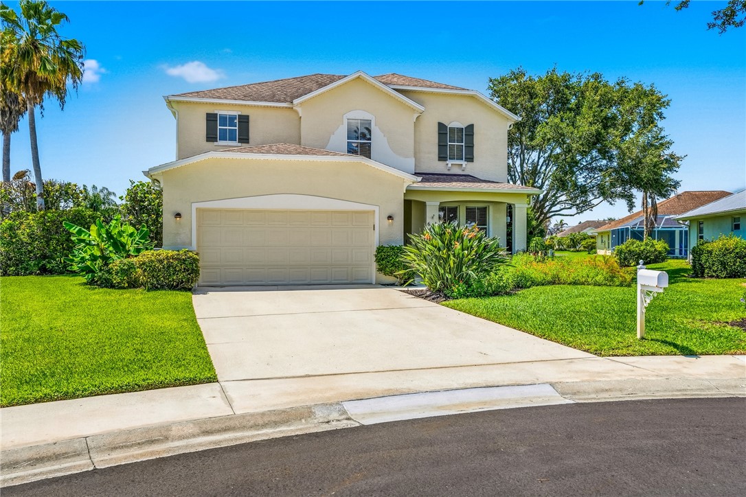 Two-story stucco residence featuring a two-car garage, mature landscaping, and a concrete driveway