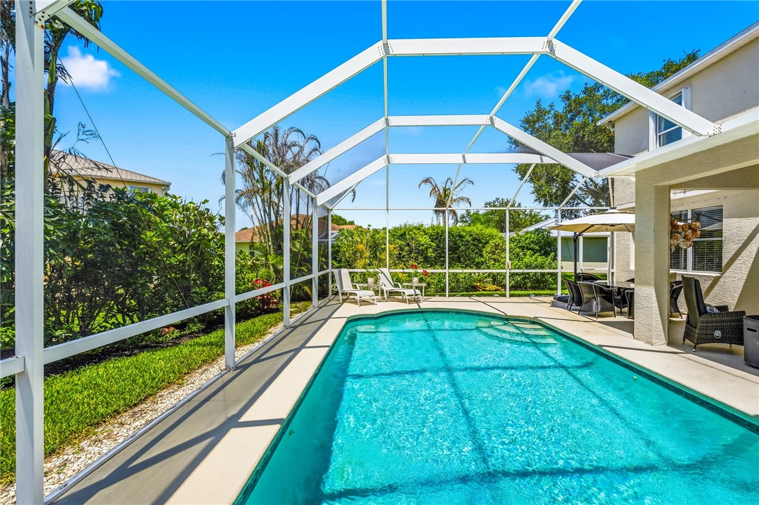 Screened pool enclosure featuring a rectangular swimming pool with integrated steps, a concrete pool deck, and mature landscaping