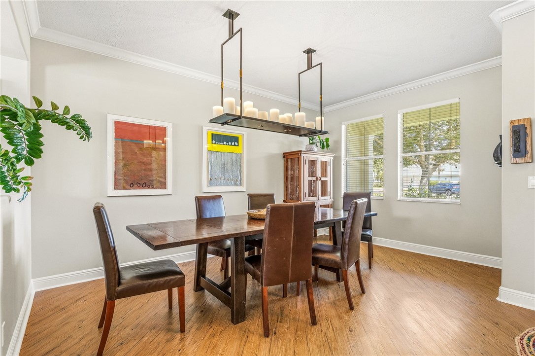 Dining area featuring wood-finish flooring, a linear chandelier, crown molding, and multiple windows