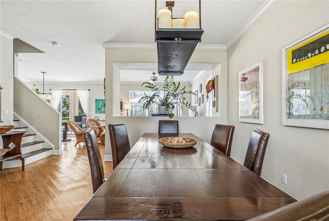 Dining area with wood-finish flooring, featuring a dark wood table, a multi-candle chandelier, crown molding, and a pass-through window to an adjacent room