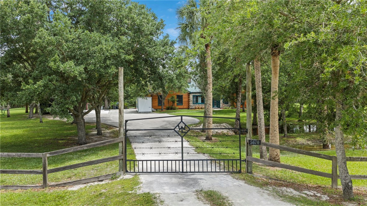 Gated entrance with a black wrought iron gate, leading to a paved driveway