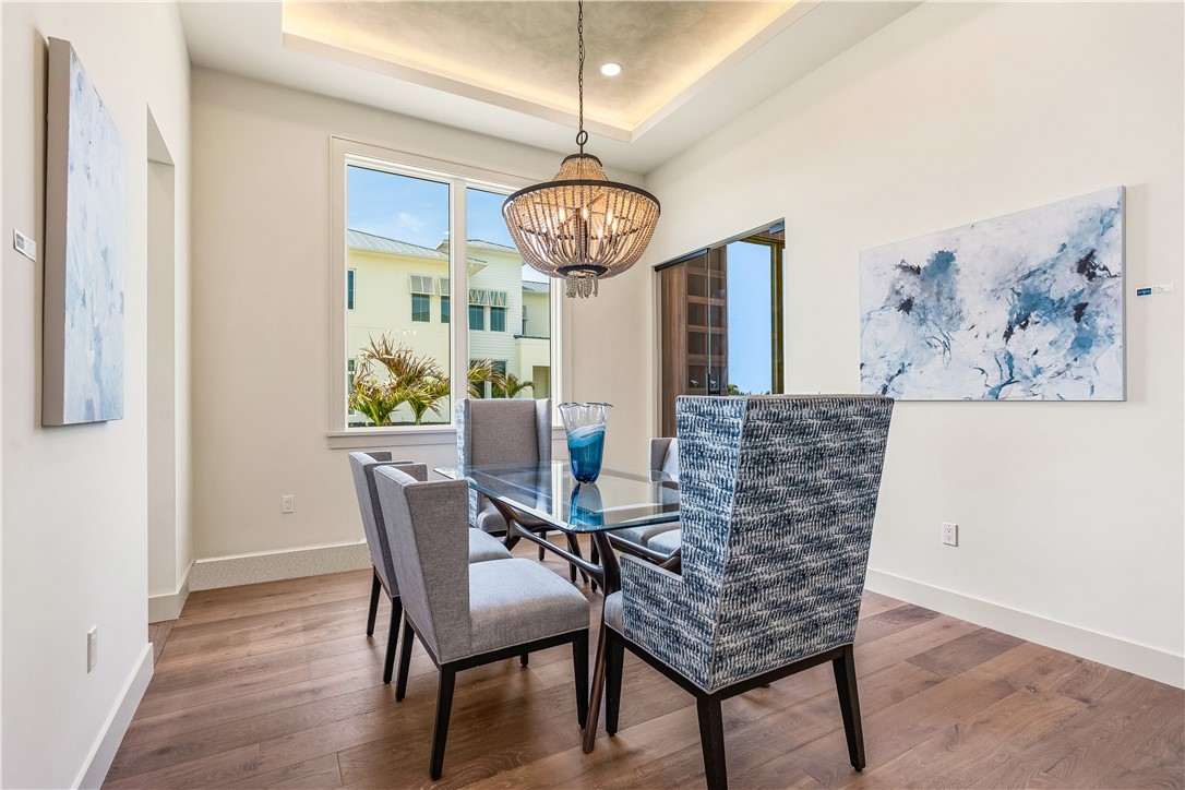 Dining area featuring wood flooring, a contemporary chandelier, and a recessed ceiling with integrated lighting