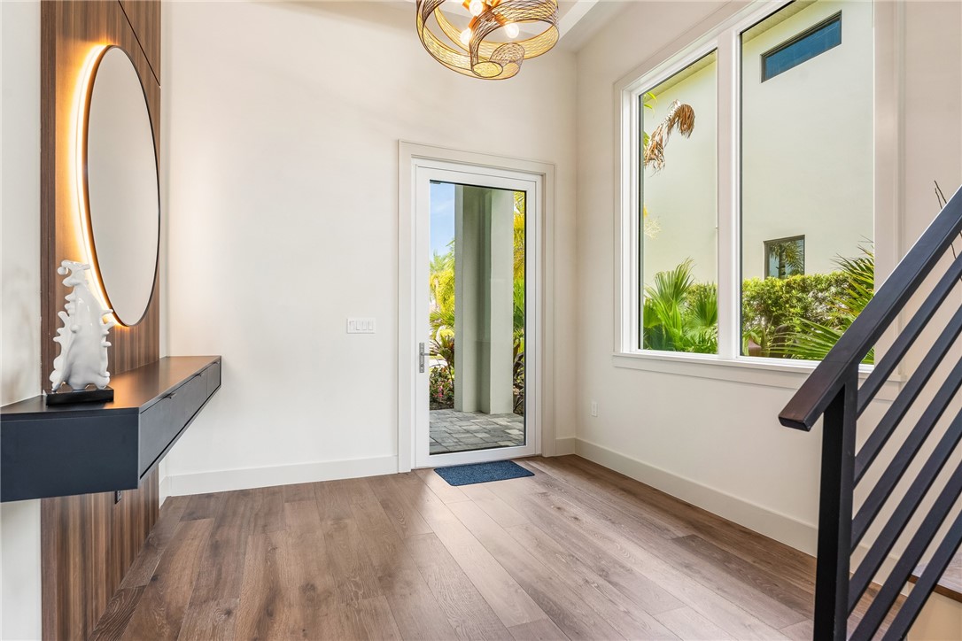 Foyer featuring wood-flooring, a full-lite entry door, and a built-in floating console with a custom designed illuminated circular mirror