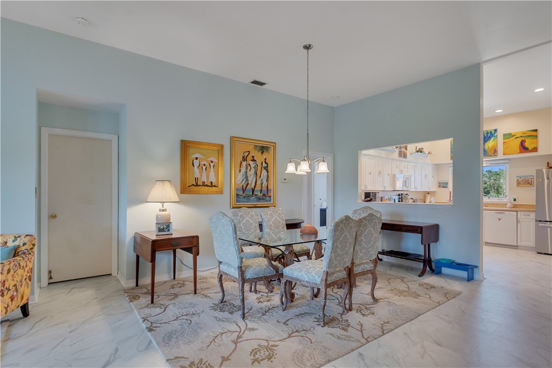 Dining area featuring a glass-top table with upholstered chairs, a decorative pendant light fixture, light blue wall paint, and white-finish flooring