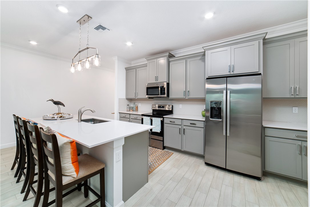 Modern kitchen featuring light gray cabinetry, stainless steel appliances, a white island with an undermount sink, recessed lighting, and wood-finish flooring