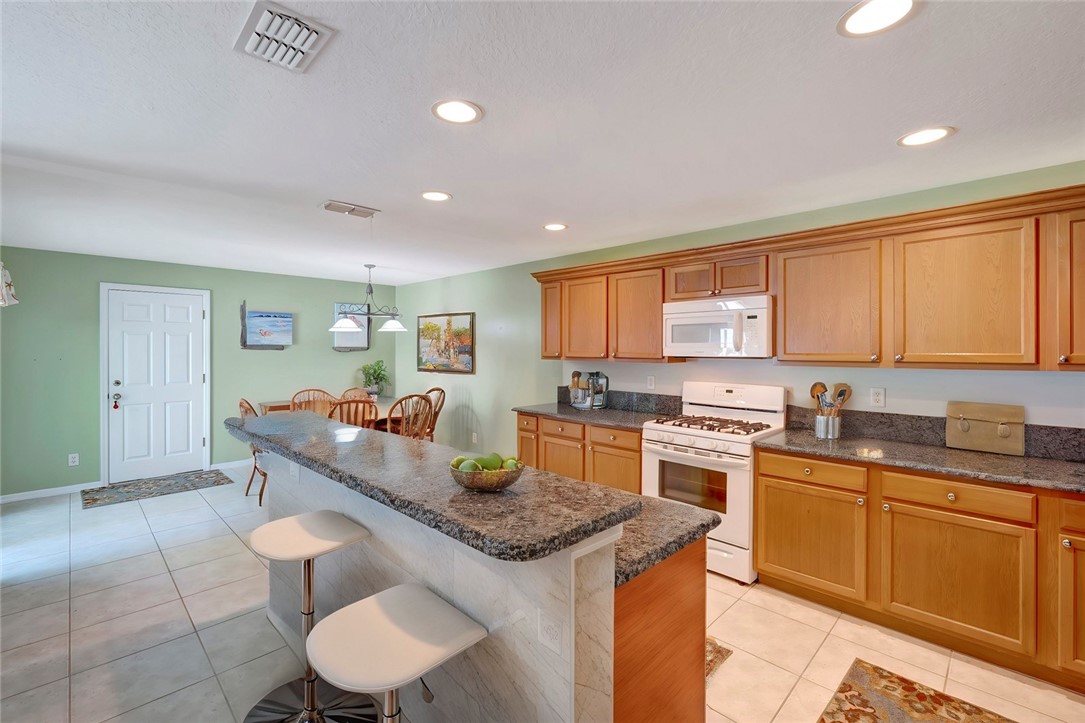 Kitchen featuring light wood cabinetry, dark granite-style countertops, and white appliances including a built-in microwave and gas range