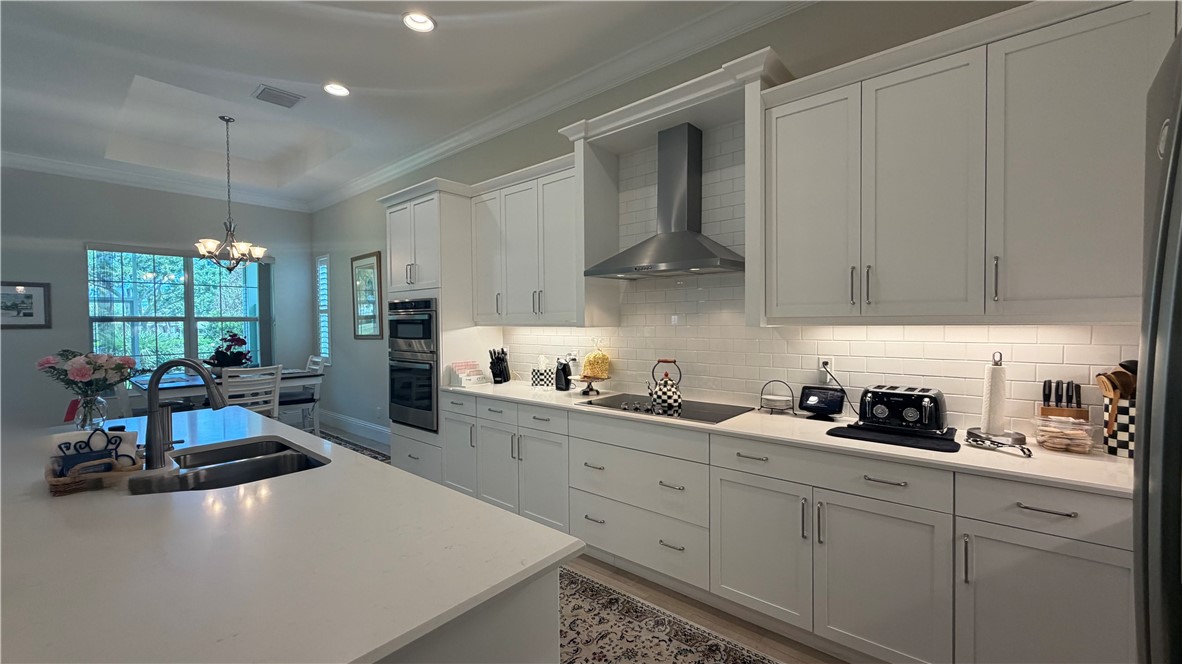 Kitchen featuring extensive white cabinetry, light-toned countertops, a stainless steel range hood, and a subway tile backsplash